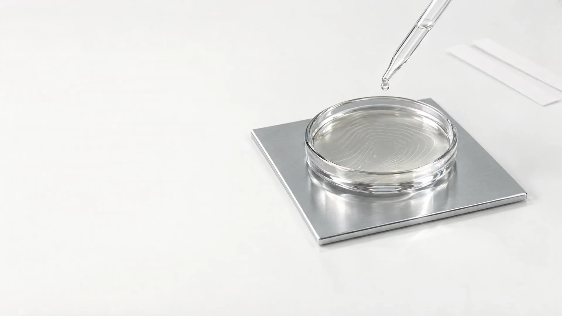 A clear fragrance droplet above etched glass and brushed chrome